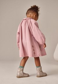 Abito di cotone rosa con maniche a sbuffo, decorato con ricami floreali sull'orlo. Abbinato a stivali alla caviglia argento e calzini verde menta.