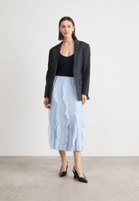 Blazer noir à rayures, haut noir à encolure dégagée, jupe à volants bleu clair superposée, chaussures compensées noires, accessoires minimalistes. Textures lisses.