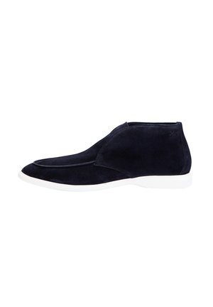 Black suede ankle boot with white sole, side profile, slip-on style, minimal stitching, and subtle logo near heel.