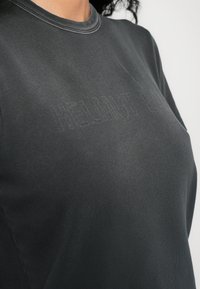 Camiseta de algodón gris con cuello redondo, que presenta un sutil logo de la marca en relieve en la parte frontal. Textura suave y corte relajado.