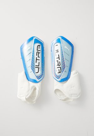 Une paire de protège-tibias de football Puma Ultra Flex bleus et blancs avec coque en plastique protectrice et manchons de cheville blancs attachés.