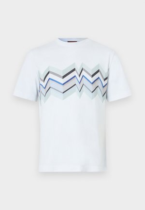 T-shirt en coton blanc arborant un motif en zigzag dans des tons de bleu, gris et vert sur la poitrine. Manches courtes et col rond.