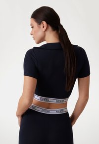 Top corto de color navy con mangas cortas, que presenta un cuello y una banda blanca con el logo en el dobladillo. Textura suave, diseño ajustado.