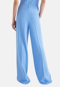 Pantaloni a gamba larga con pannelli in tessuto blu chiaro; presentano una superficie liscia, vita e dettagli della tasca posteriore.