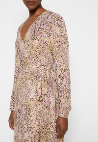 Femme portant une robe portefeuille à manches longues et décolleté en V, avec un motif imprimé animal rose, beige, noir et blanc, se nouant à la taille.