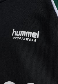 Svart tyg med vitt "hummel"-logotyp och texten "SPORTSWEAR"; har en slät textur och en ren design, lämplig för sportkläder.