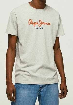 Mężczyzna ubrany w jasnoszarą koszulkę z krótkim rękawem z napisem "Pepe Jeans London" w kolorze pomarańczowym i niebieskim, w połączeniu z niebieskimi dżinsami.