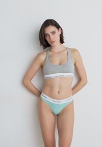 Grå sports-bh med en hvit Calvin Klein-logo band og lyseblå truse med hvit midjebånd. Glatt stoff, tettsittende design.