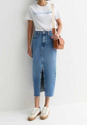 Jupe midi en denim avec fente avant et ourlet effiloché, associée à un t-shirt blanc avec texte bleu et baskets beiges. Sac en bandoulière tan inclus.
