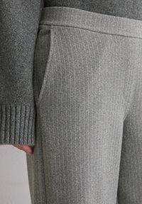 Pantalon gris à fines rayures avec une texture douce, doté d'une large ceinture et de poches latérales, présenté aux côtés d'un pull en maille.