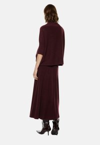 Maglione a maglia bordeaux con maniche corte e orlo a coste, abbinato a una gonna a coste coordinata, indossato con stivali neri lucidi alla caviglia.