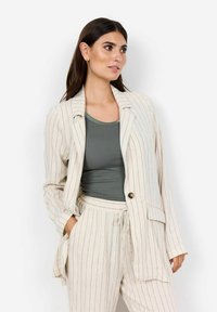 Leicht beiges gestreiftes Blazer mit lockerer Passform, einreihigem Knopfverschluss und zwei Seitentaschen, kombiniert mit einem taillierten grünen Tanktop.