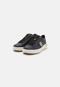 Black leather sneakers with a textured finish, white rubber sole, gold eyelets, and a decorative logo on the side. Flat laces included.
