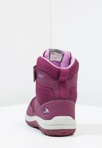 Bota infantil morada con tejido texturizado, correa ajustable y cuello acolchado. Presenta una suela blanca con agarre antideslizante.