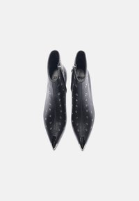 Botas de cuero negras hasta el tobillo con puntas afiladas, acentos de tachuelas plateadas y cierre de cremallera en el costado. Textura suave con detalles metálicos.