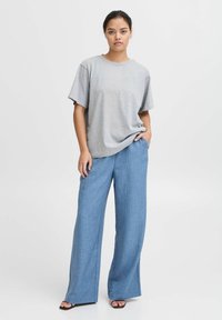 Grå t-shirt med kort ärm som kombineras med ljusblå vida byxor i en texturerad tyg. Svarta slidesandaler fulländar outfiten.