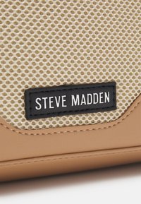 Šviesus maišelis su tekstūruota kreminės spalvos tinklo juostele ir juodos odos etiketė, ant kurios balta rašyba yra užrašyta "STEVE MADDEN".