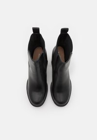 Botas de tobillo de cuero negro con paneles laterales elásticos, puntera redondeada y lengüetas traseras para ponerlas fácilmente. Textura suave y diseño minimalista.