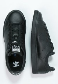 Svarta sneakers i läder med en slät yta, perforerade sidopaneler, rund tå och svarta snören. Har en vit Adidas-logotyp på tungan.