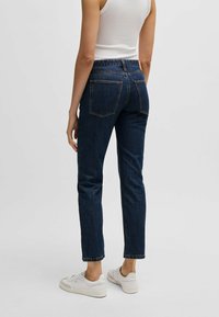 Tummanpesun farkut slim fit -mallilla, viisi taskua ja kontrastiväriset tikkaukset. Yhdistetty valkoisten lenkkareiden ja tiukan toppatuden kanssa.