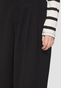 Pantalon noir avec une texture lisse et des détails plissés. Assorti à une chemise à rayures à manches longues, affichant une coupe décontractée.
