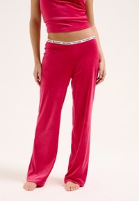 Pantaloni lounge rosa a coste con vestibilità rilassata e cintura elastica con il nome del marchio. Tessuto morbido e design a lunghezza intera.