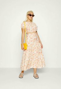 Conjunto de duas peças com um top cropped e uma saia longa com um padrão floral em pêssego e branco. Os acessórios incluem uma bolsa amarela e sandálias.