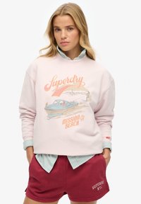 Lichtroze sweatshirt met grafische print van een boot en de tekst "Superdry Mission CA Beach". Gepaard met bordeauxrode shorts en een gestreepte kraagshirt.