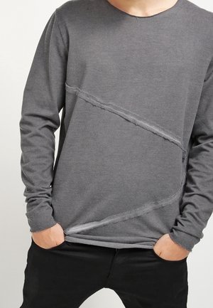 Grijs shirt met lange mouwen gemaakt van zachte stof, met diagonale verweerde details en een ronde halslijn. Gecombineerd met een zwarte broek.