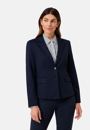 Marineblauer Blazer mit taillierter Passform, einem einzelnen Knopfverschluss und zwei Fronttaschen, kombiniert mit einem weißen und marineblauen gestreiften Hemd darunter.