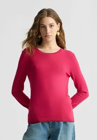 Figurbetontes, magentafarbenes Langarmstricktop mit Rundhalsausschnitt und gerippten Details an den Bündchen und dem Saum. Glatte Textur, kombiniert mit Jeans.