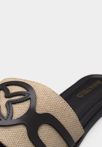 Κοντινό πλάνο μιας μπεζ πλεχτής σαγιονάρας με μαύρη διακοσμητική λωρίδα με κοψίματα και μαύρη σόλα.