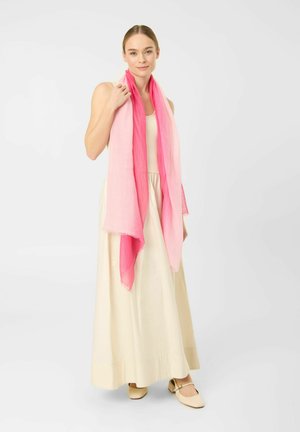 Woman wearing a sleeveless cream maxi dress, beige shoes, and a long pink gradient scarf draped around her neck and shoulders.