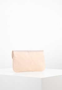 Beige psaníčko s jemnou semišovou texturou, vyznačující se metalickým, třpytivým lemem podél horního okraje. Obdélníkový tvar, minimalistický design.