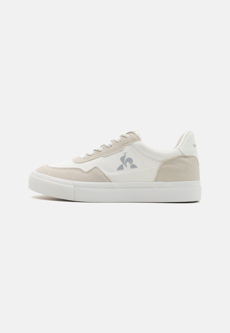 Sneakers blanches et beiges avec une tige en cuir lisse et des accents en daim. Présente des sections perforées et un logo sur le côté. Semelle en caoutchouc épaisse.