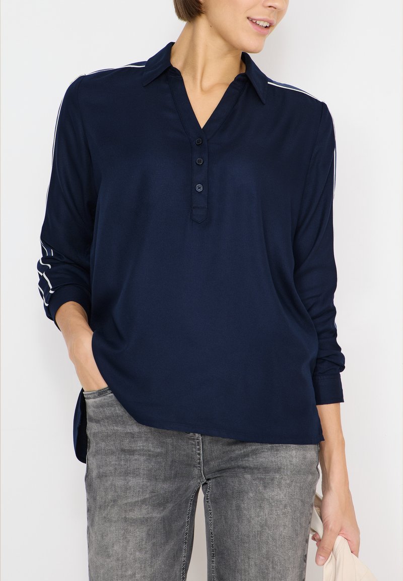 Camicia a maniche lunghe blu navy con colletto, tre bottoni e strisce bianche sulle maniche. Tessuto liscio e vestibilità ampia.