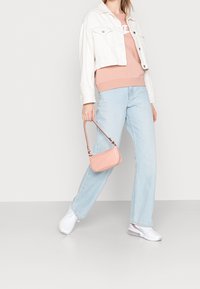 Vit denimjacka, persikofärgad sweatshirt, ljusblå vida jeans, vita sneakers och en liten rosa handväska. En enkel och avslappnad outfit.