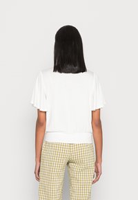 Weißes Kurzarmoberteil mit lockerer Passform und geripptem Saum. Kombiniert mit grün-beige karierten Hosen mit einer entspannten, glatten Textur.