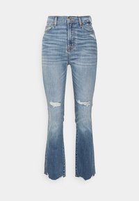 Pantalones vaqueros de denim azul de cintura alta con desgarros en las rodillas y dobladillos acampanados, que presentan un clásico diseño de cinco bolsillos y herrajes dorados.