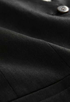 Tissu noir avec une texture lisse, présentant un motif de tissage diagonal et un détail de bouton. Le matériau semble durable et bien cousu.