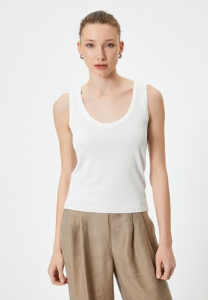 Top de tirantes ajustado en blanco con escote redondeado y tirantes anchos. Textura suave con dobladillo acanalado. Combinado con pantalones fluidos de color marrón claro.