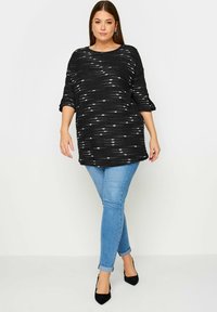 Svartvit mönstrad stickad topp med lös passform och trekvartslånga ärmar, tillsammans med ljusblå skinny jeans och svarta klackar.