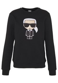 Felpa nera con una figura cartoon con capelli bianchi, occhiali da sole e un completo, centrata sulla parte anteriore. Tessuto morbido con polsini a coste.