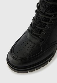 Svarta ankelboots med en texturerad läderöverdela, perforerad tå, tygfoder och en tjock gummisula med ett robust mönster.