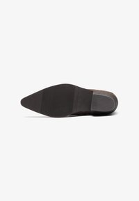 Suela de zapato de cuero negro con un diseño de punta afilada, agarre de goma texturizada y un ligero tacón. Presenta un acabado mate suave.
