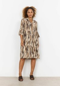 Abito midi a motivo marrone e beige con scollatura a V, maniche a tre quarti e design a strati, abbinato a scarpe con tacco a blocco marroni.