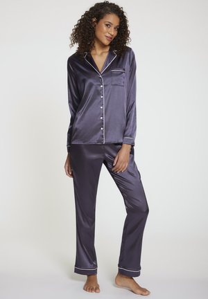 Pigiama di raso blu navy con piping bianco, composto da una giacca con bottoni, maniche lunghe e pantaloni abbinati alla caviglia con dettagli sulle tasche.
