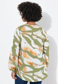 Blusa verde con un motivo astratto bianco e arancione, maniche lunghe a sbuffo e scollatura tonda. Tessuto morbido con una sottile texture.
