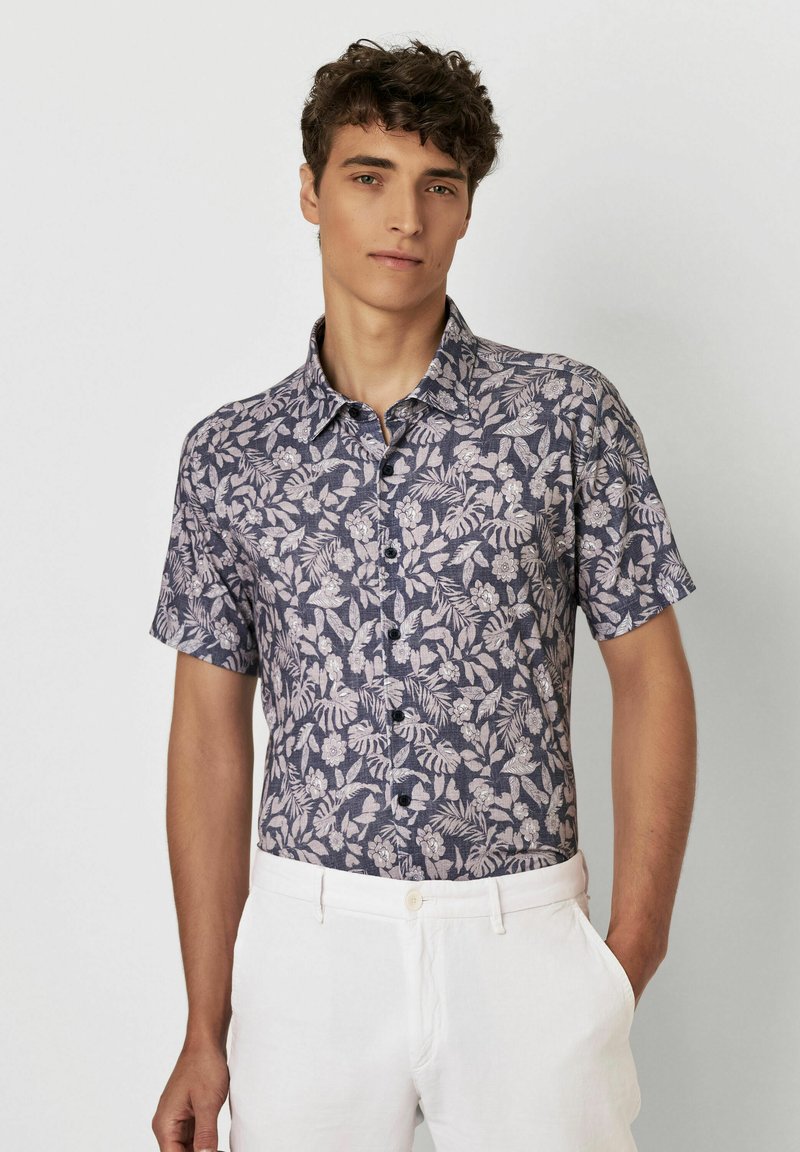 Kurzarmhemd aus dunkelblauem Stoff mit einem floralen Muster in Hellrosa. Mit Knopfleiste und spitzem Kragen.