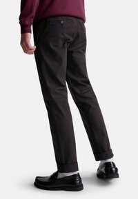Pantalon en coton noir avec une coupe ajustée, présentant des poignets retroussés, des poches arrières avec bouton, associé à des mocassins noirs et des chaussettes grises.